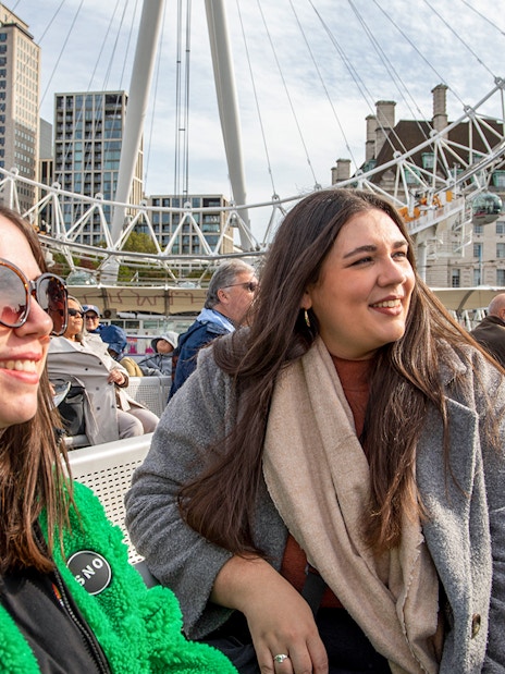 Women enjoying Thames River afternoon cruise with London Eye in the background.
