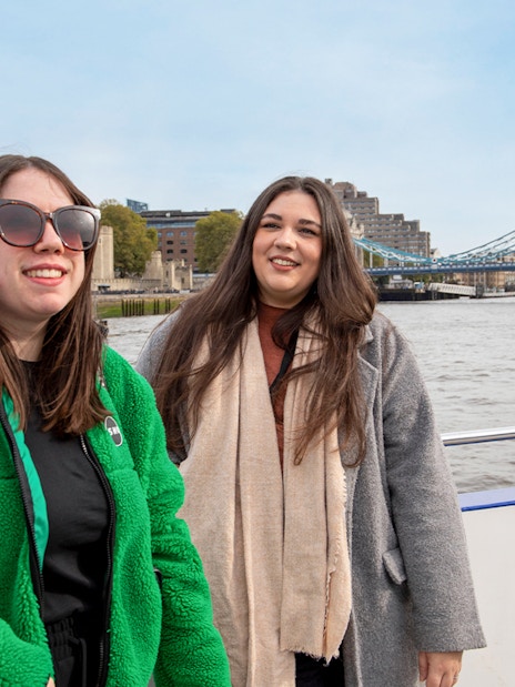 Women enjoying Thames River afternoon cruise with view of London Eye and cityscape.