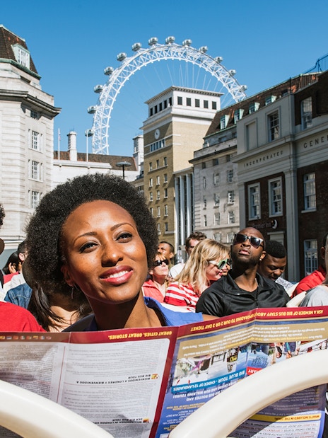 Tourists on BigBus London tour passing the London Eye, enjoying hop-on-hop-off experience with Thames River Cruise.
