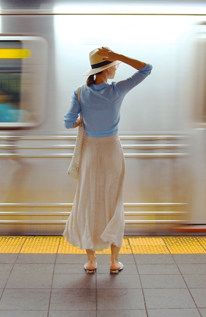 Girl waiting on a railway platform with a suitcase in hand, cityscape in the background.