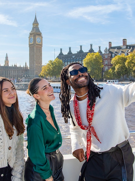 Friends enjoying a Thames River cruise with iconic London landmarks in the background.