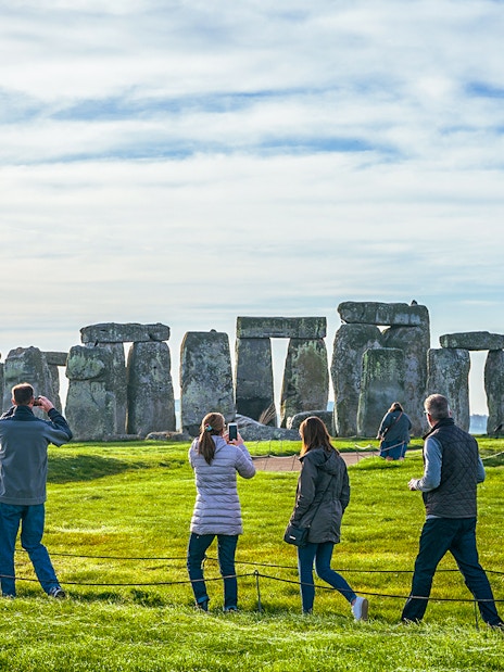 Tourists at Stonehenge, ancient stone structures, green fields, clear sky, day trip from London.