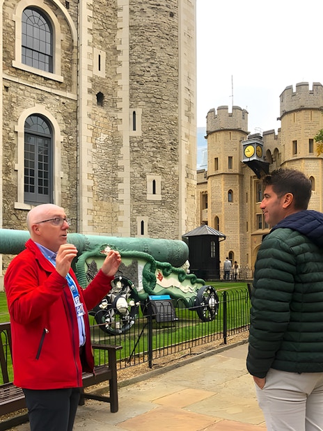 Tower of London Beefeater leading guided tour with visitors near historic fortress walls.