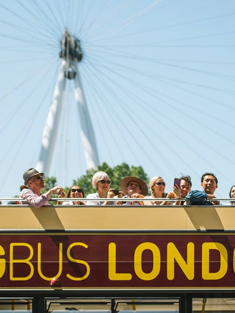 Big Bus tour in London passing the London Eye with Thames River cruise in view.