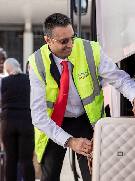man from crew loading luggage for the passengers onto a National Express Bus