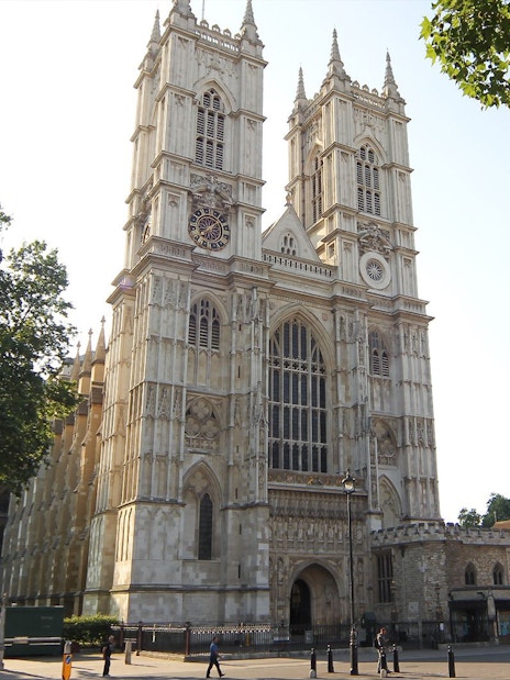Westminster Abbey exterior with tourists and iconic London red bus in the foreground.