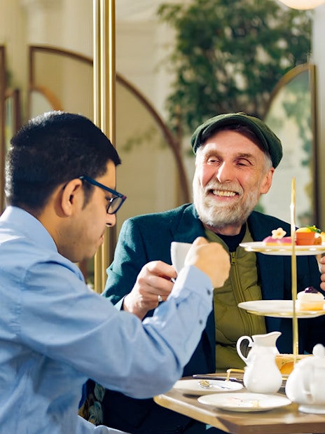 Visitors enjoying Kensington Palace afternoon tea setup with elegant tableware and pastries.