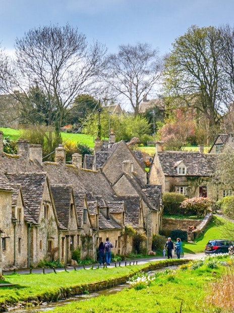 Arlington Row cottages in Bibury Village, Cotswolds, with lush greenery and a serene pathway.