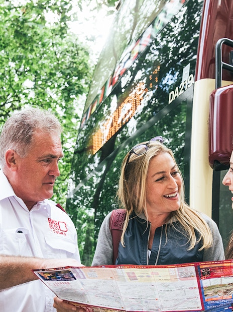 Big Bus employee assisting tourists near iconic London landmarks.
