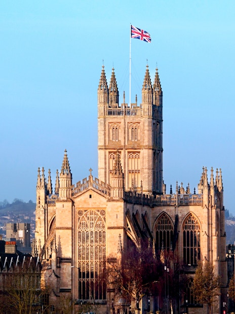 Tour group exploring Stonehenge with exclusive walk between the stones experience, departing from London, with a scenic view of Bath Abbey in the background